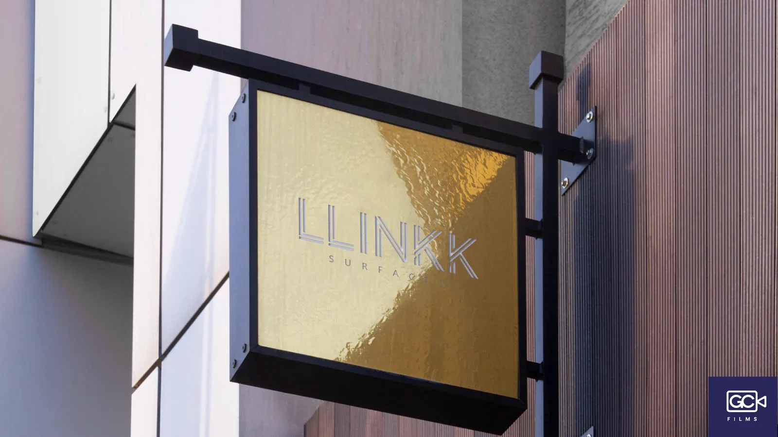 Placa suspensa em fachada de prédio comercial com o logotipo em dourado.