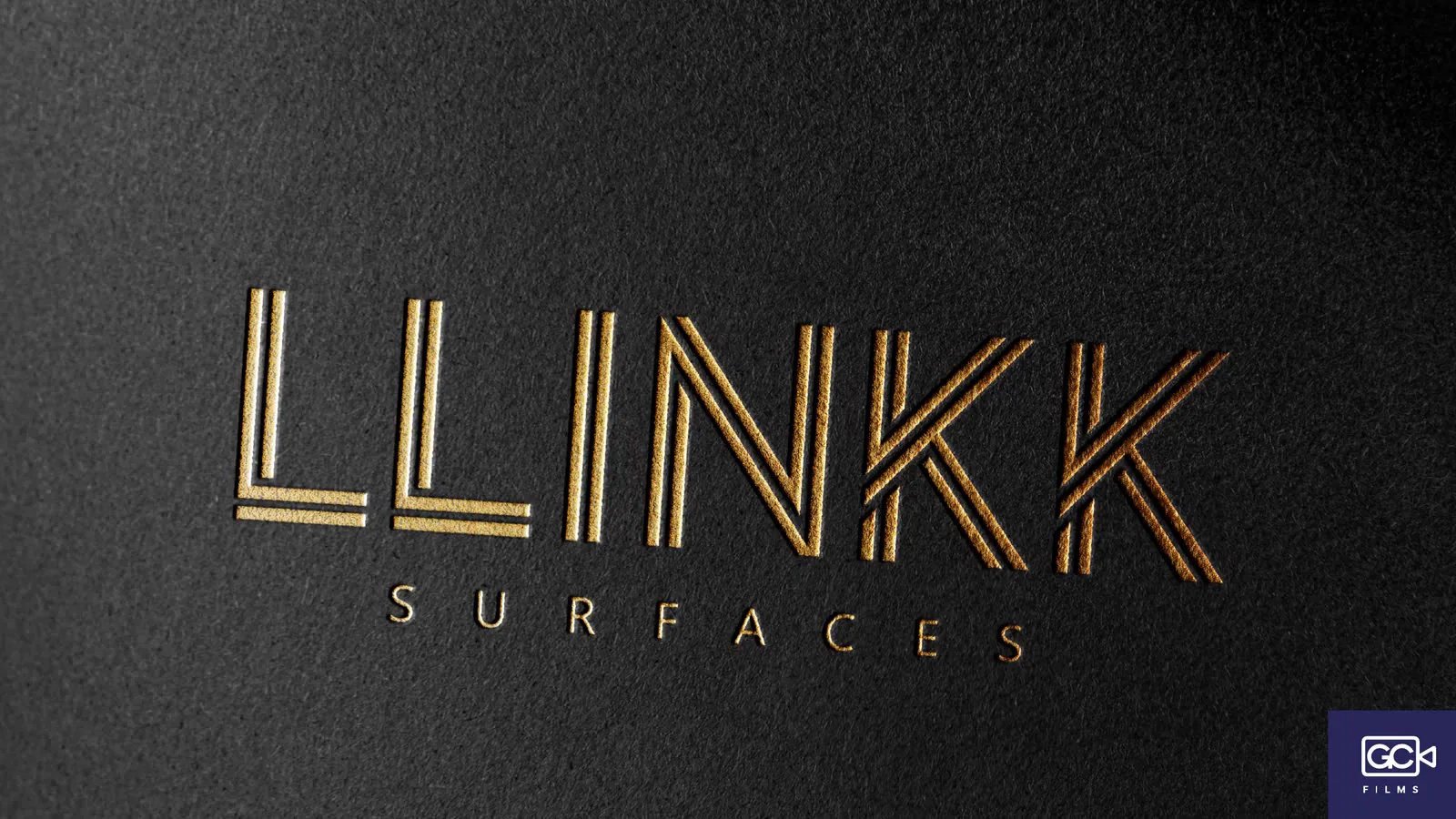 Logotipo dourado sobre papel preto texturizado, em close.