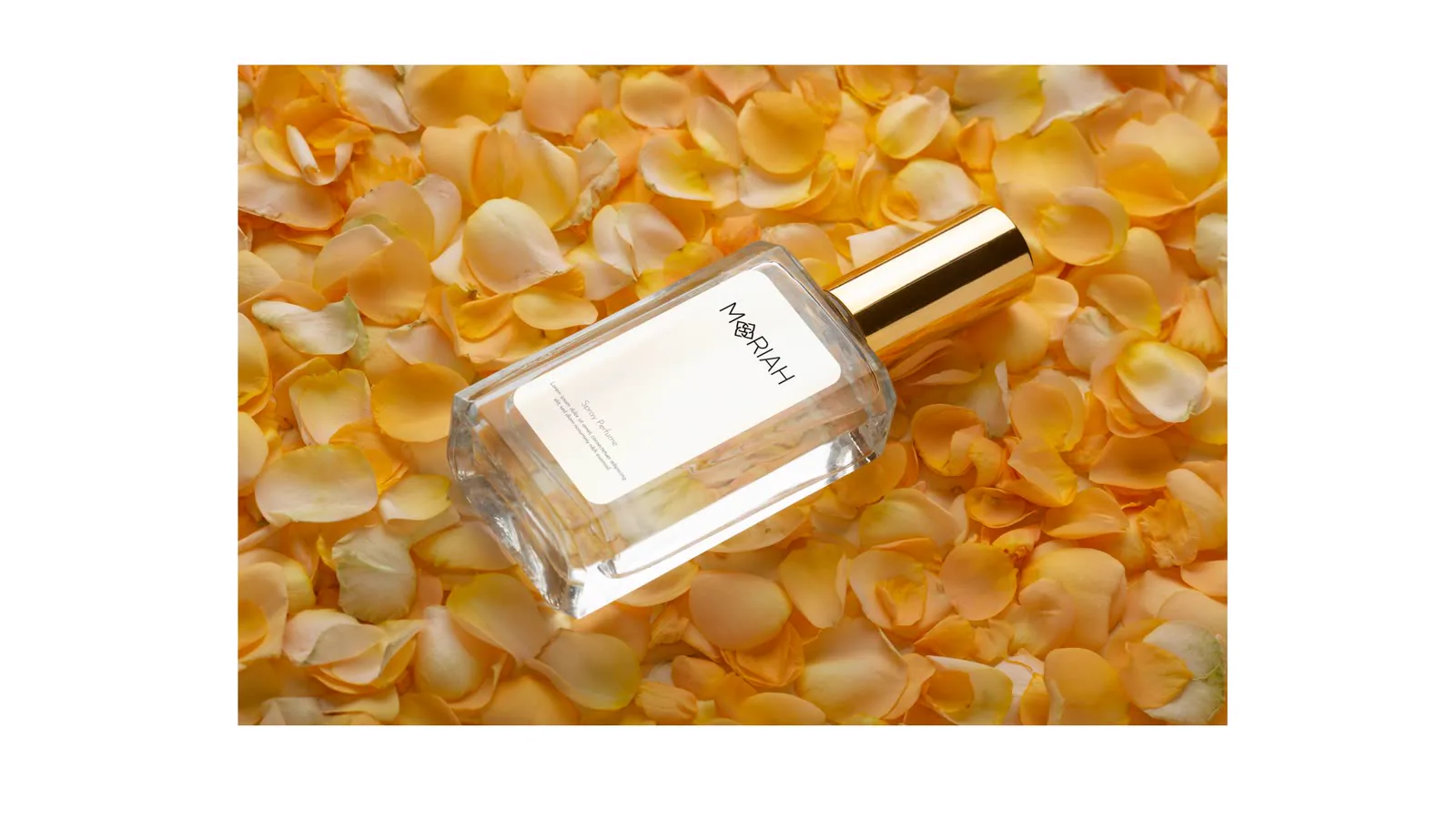 Frasco de perfume deitado sobre pétalas douradas.
