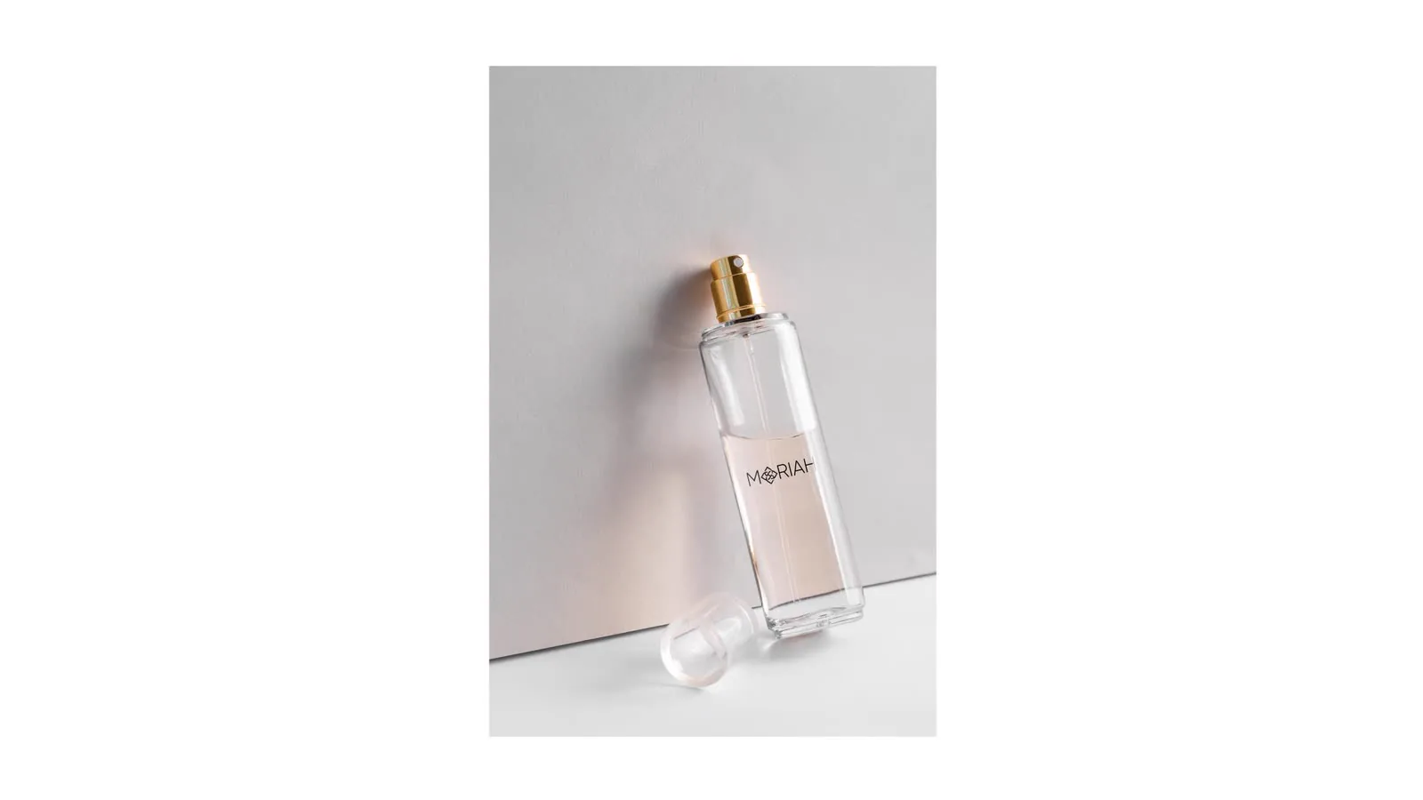 Frasco de perfume em pé sobre fundo rosado, iluminado de lado.